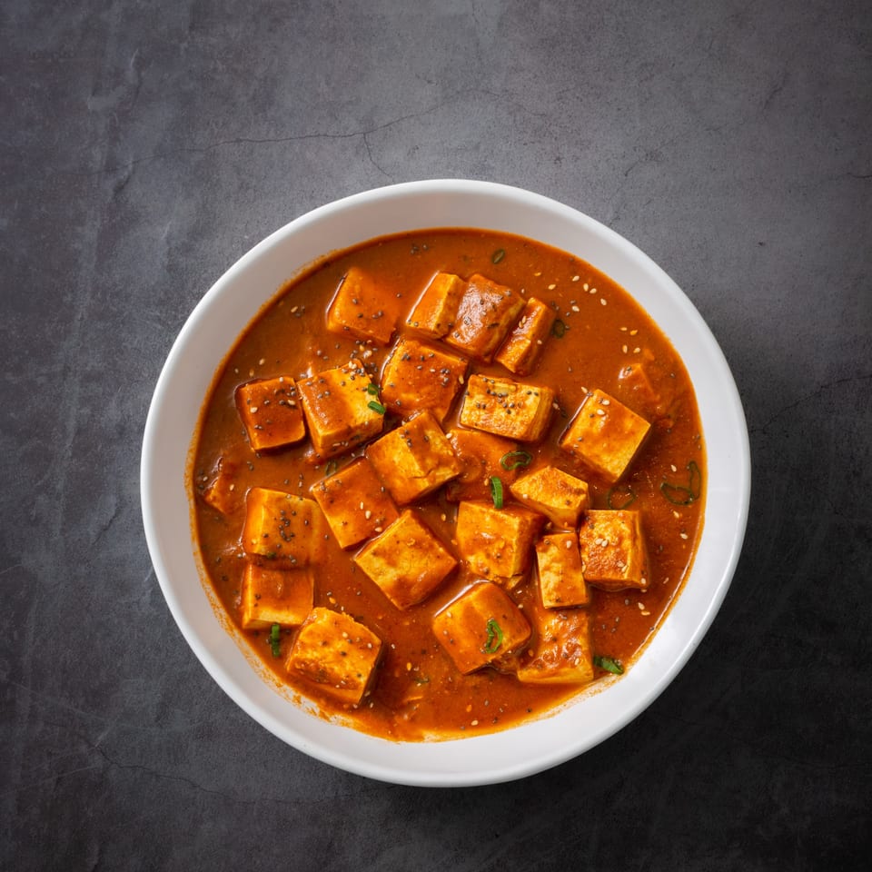 Overhead view of KS Kitchen's paneer curry, with paneer cubes in a rich orange sauce, garnished with seeds.