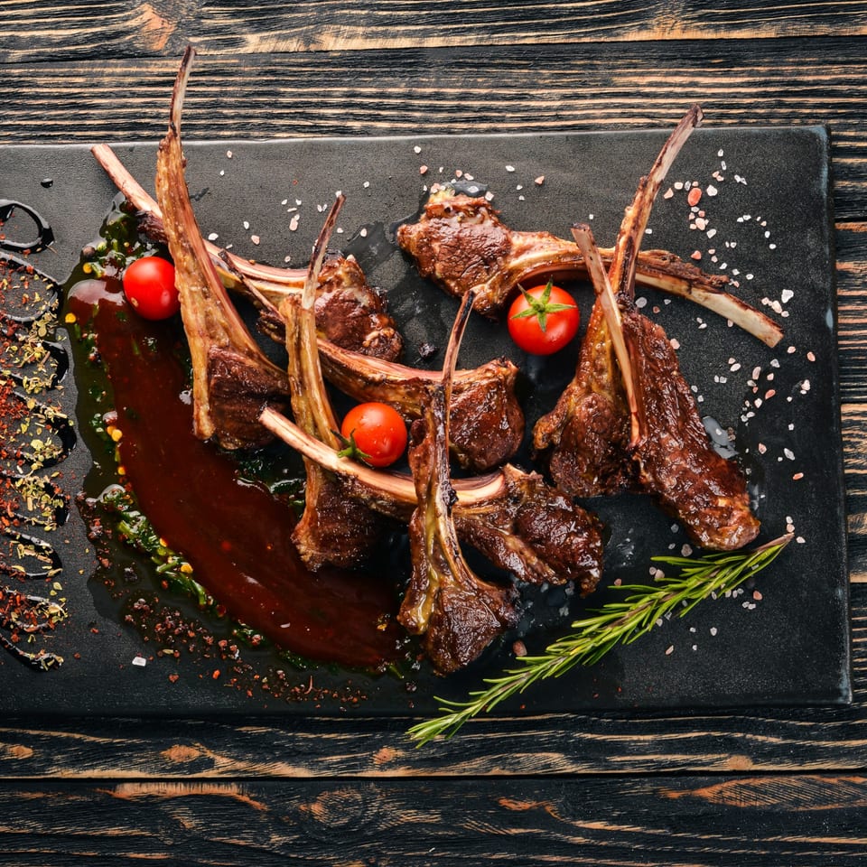 Grilled lamb chops with cherry tomatoes, rosemary, and sauce on a black plate at KS Kitchen.