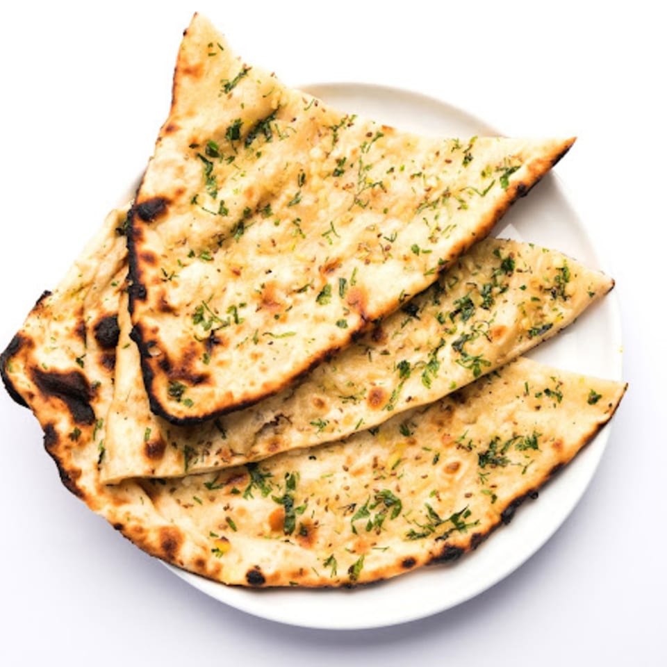 Golden-brown garlic naan bread, garnished with fresh green herbs, served on a white plate.