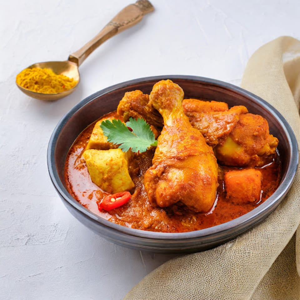 Indian chicken curry with potatoes, garnished with cilantro and chili, beside a spoon of turmeric.