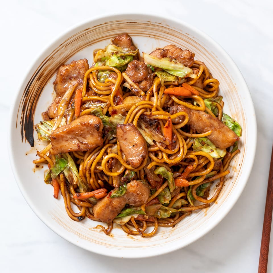 KS Kitchen's Indian stir-fried noodles with chicken, cabbage, and carrots in a white bowl.